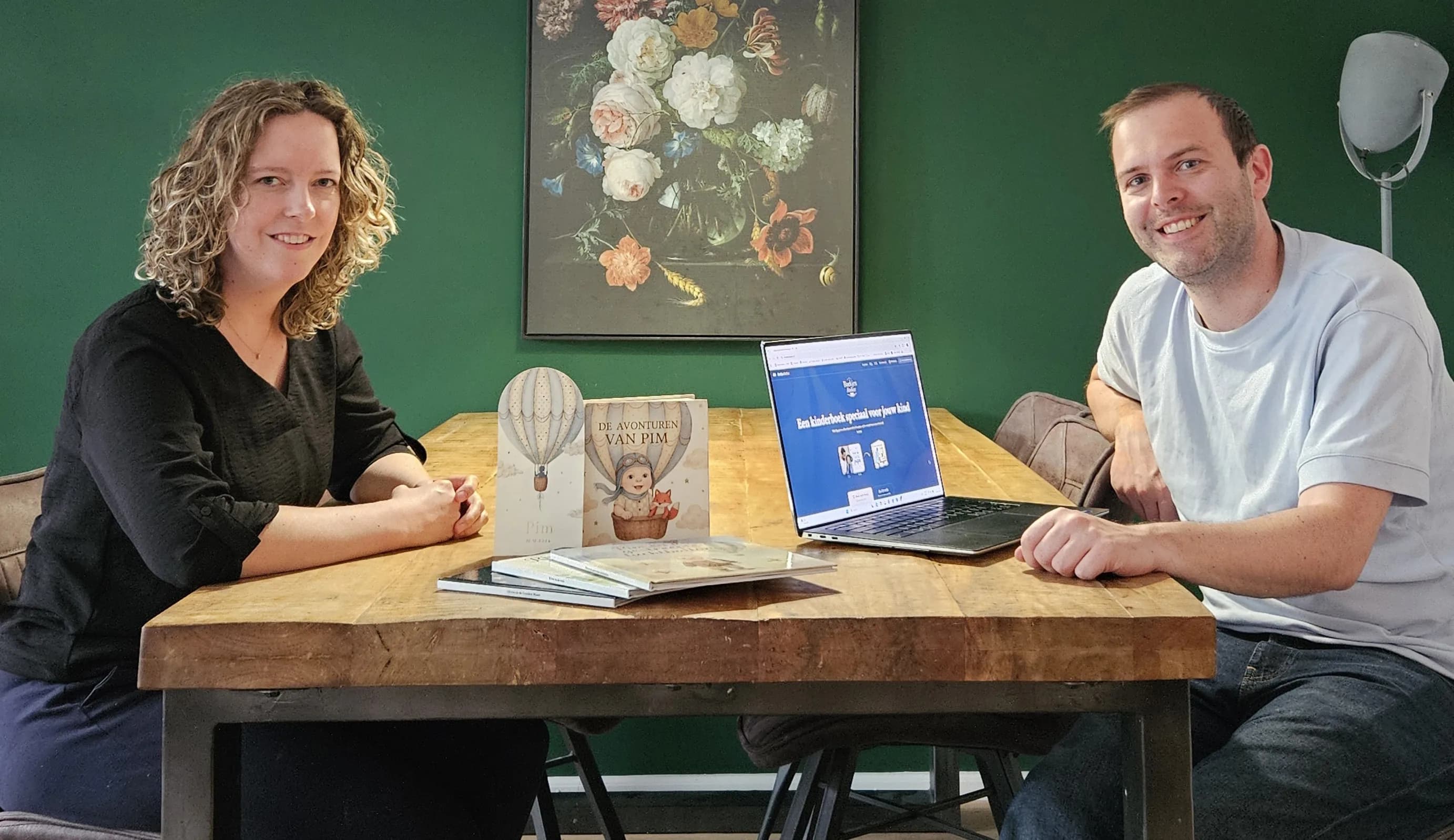 Lisa Kasius en Wouter Ouwens zitten aan tafel met het eerste boekje van Pim en de website van BoekjesAtelier op een laptop